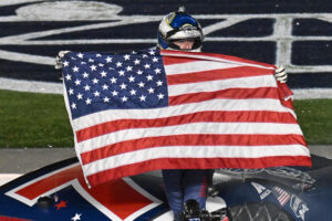 CONCORD, NORTH CAROLINA - MAY 29: Justin Allgaier, driver of the #7 Unilever Military DeCA RCPT Chevrolet, celebrates with the American flag after winning the NASCAR Xfinity Series Alsco Uniforms 300 at Charlotte Motor Speedway on May 29, 2023 in Concord, North Carolina. (Photo by Logan Riely/Getty Images)